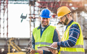 facility management, construction, technical facility management, two men with hard hats in the front and a construction site in the back 